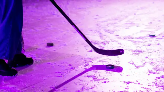 A hockey stick and pucks in the snow under purple light